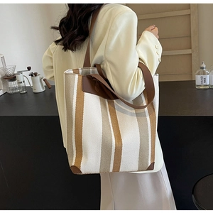 Vertical striped canvas tote bag with brown leather straps worn on a beige blazer