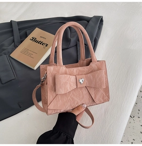 Detailed view of pink wrinkled leather handbag featuring a large bow and heart rhinestone