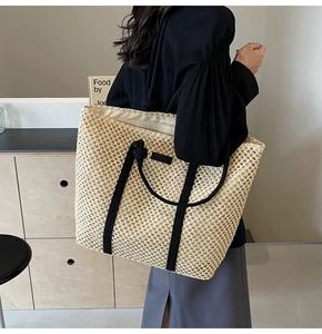 Detailed view of the hollow woven straw tote bag featuring black rope handles and leather patch