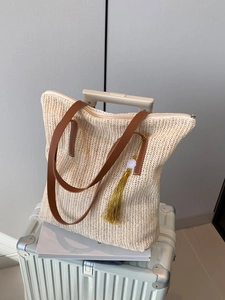 Sac cabas en paille beige avec anses en cuir marron et pompon en soie sur une valise