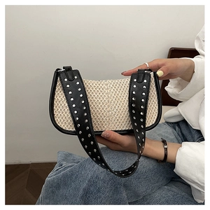 Détail du sac croissant en paille tressée avec rivets argentés sur la bandoulière noire