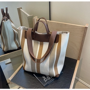 Detail view of the brown leather handles and striped canvas material on the tote bag
