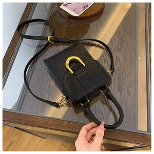 Close-up of black wrinkled leather texture and golden D-shaped metal clasp on the handbag