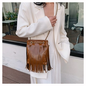 Détail d'un sac seau marron à franges avec bandoulière chaîne et longs pompons d'ornement
