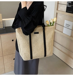 Detail showing handwoven texture and black shoulder straps of a beige straw tote bag