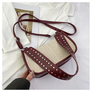 Détail du sac en paille tissée avec cuir bordeaux et rivets métalliques sur la bandoulière