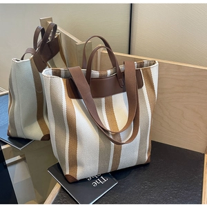 Detailed view of stripe canvas tote bag with reinforced leather corners on wooden steps