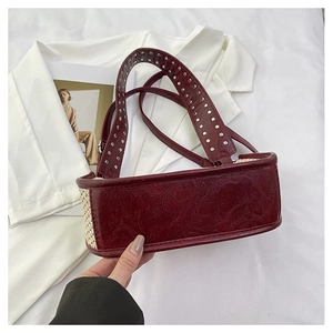 Détail de la poignée en cuir bordeaux avec rivets argentés sur le sac tissé beige