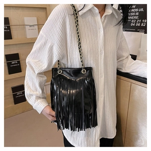 Détail du sac seau en cuir noir avec de longues franges et une bandoulière en chaîne dorée