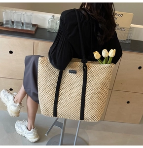 Detail of a large straw tote bag with black strap handles and a minimalist black patch