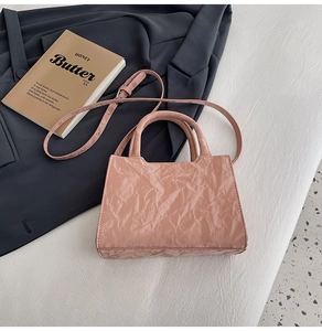 Detailed close-up of pink wrinkled texture small handbag with dual handles and strap