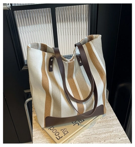 Close-up of a striped canvas tote bag with brown leather handles and reinforced bottom