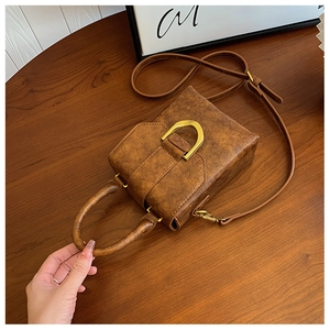 Close-up of vintage brown leather mini box bag with gold D-ring buckle on wooden table