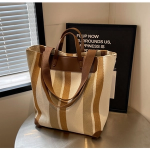 Close-up of contrast striped canvas tote bag with brown leather handles on a metal table