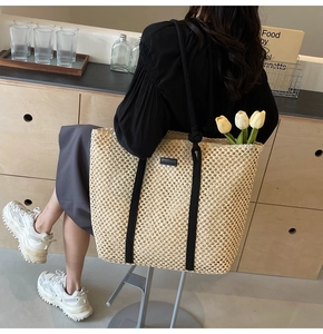 Close-up of beige hollow-out woven tote bag featuring thick black rope shoulder straps