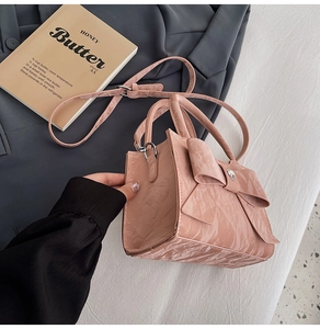 Detail of pink bow handbag with heart hardware on a grey blazer and book background