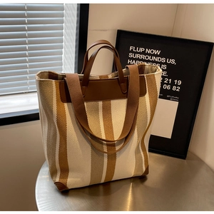 Detail of striped canvas tote bag featuring leather handles and reinforced corner patches