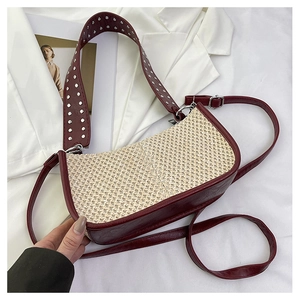 Détail de la texture paille beige et cuir bordeaux avec rivets argentés sur la sangle