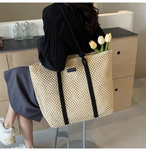 Detail view of a large woven straw tote bag featuring black straps and tulip decorations