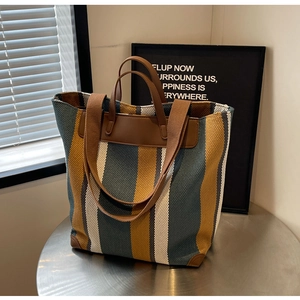 Detail of color-block striped canvas tote bag with brown leather handles on a metal table