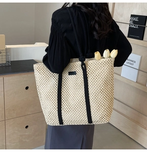 Detail of hollow woven straw tote bag featuring black stripes and rope handles for beach
