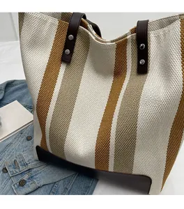 Close-up of contrast striped canvas tote bag with brown leather handles and silver rivets