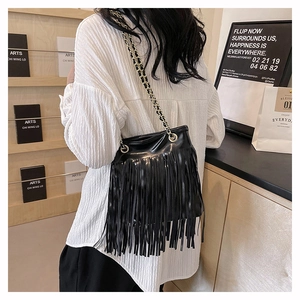 Sac à bandoulière noir à franges avec chaîne en métal porté par un mannequin en intérieur