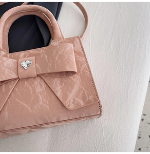 Detail of light pink mini bag with textured fabric, large bow, and heart-shaped crystal