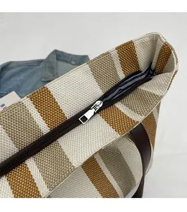 Detail of smooth zipper closure and leather handle on a striped canvas tote bag