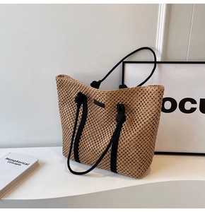 Detailed macro view of woven straw tote bag with black cotton rope handles and leather label