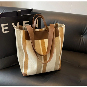 Detail view of striped canvas tote bag with leather straps on a dark leather sofa