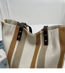 Close-up of contrast striped canvas tote bag with brown leather handles and metal rivets