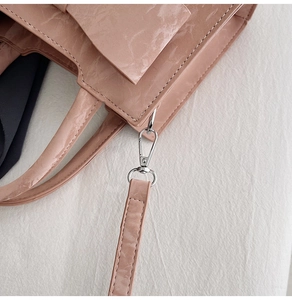 Detail of pink bow handbag with pleated texture and silver metal swivel snap hooks