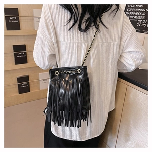 Détail d'un sac seau noir à franges avec bandoulière en chaîne dorée sur un mannequin