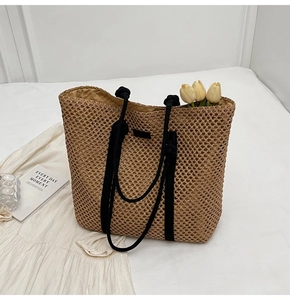 Detail of hollow woven straw tote bag with black rope handles and mesh texture