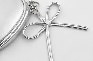 Close-up of silver leather mini bag showing bow charm detail and precise stitching