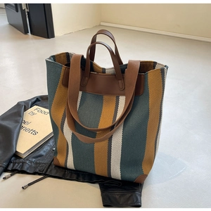 Detail of striped canvas tote with leather handles and reinforced base on a minimalist setup