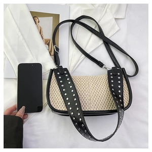 Sac hobo en paille avec rivets argentés et bordure en cuir noir près d'un smartphone