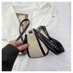 Détail du sac tressé beige avec bandoulière en cuir noir ornée de rivets argentés élégants