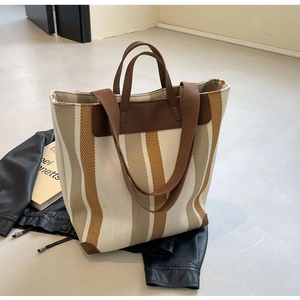 Detail of canvas tote bag featuring brown vertical stripes and premium leather straps