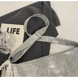 Detail of silver cracked leather bucket bag with white lace ribbon on suit jacket