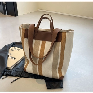 Detailed view of large canvas tote bag with colorful vertical stripes and leather trim