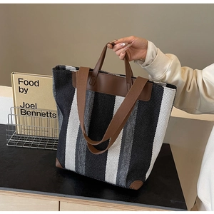 Detail of black and white striped canvas tote bag with brown leather handles and corners