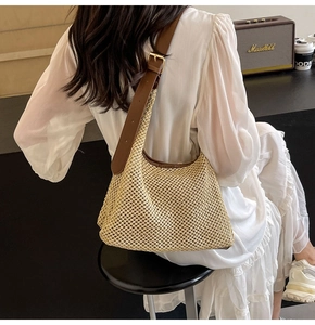 Close-up of a woven shoulder bag with brown leather strap and golden metal hardware