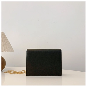Close-up of black lychee grain flap bag with gold chain strap on a minimalist white surface