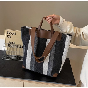 Close-up of striped canvas tote bag with brown leather details and woven shoulder strap