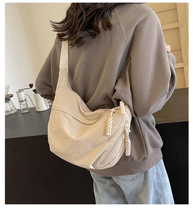 Détail du sac demi-lune en nylon beige avec fermeture à nœud et large bandoulière