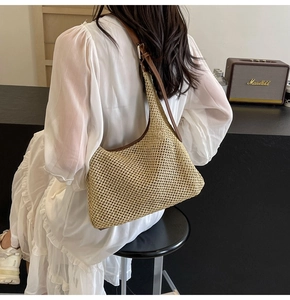 Detail of woven straw shoulder bag featuring brown leather strap and elegant crescent shape