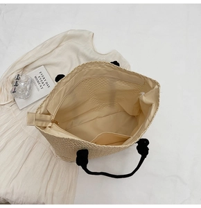 Close-up of woven straw tote bag featuring black rope handles and interior zipper pocket