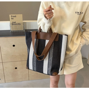 Detail of canvas tote with black stripes and brown leather corners on a wooden background